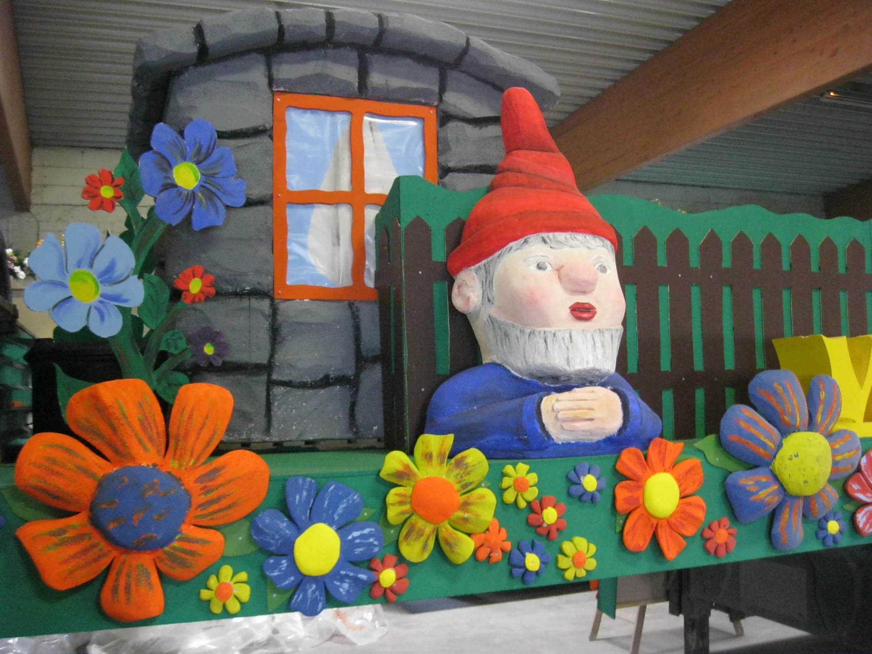 Nahaufnahme eines bemalten Zwergs mit bunten Blumen und einer gemalten Kulissenwand